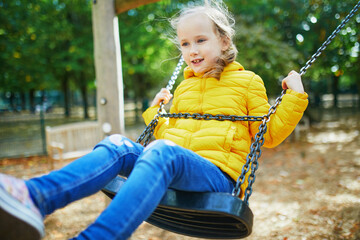 Happy 6 years old girl on a swing. Happy kid on playground swinging on seesaw. Outdoor autumn activities for children