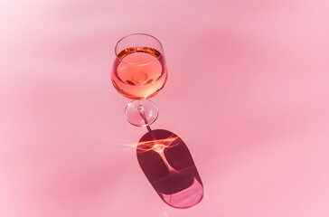 Pink wine in a transparent glass on a modern pink background, top angle view, minimalistic, studio shot. Design concept