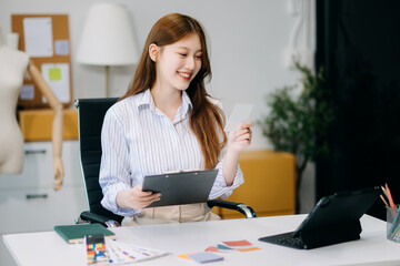 Fashion designer woman talking smart phone and using laptop with digital tablet computer in modern studio