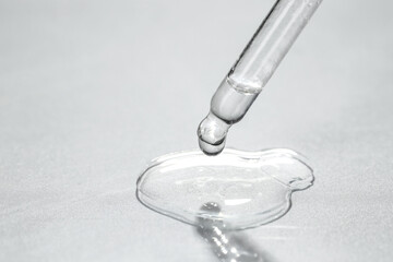 Sticker - Cosmetic oil dripping from pipette on light grey background, closeup