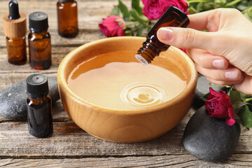 Sticker - Woman dripping essential oil into bowl with water at wooden table, closeup