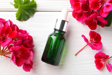 Poster - Bottle of geranium essential oil and beautiful flowers on white wooden table, flat lay