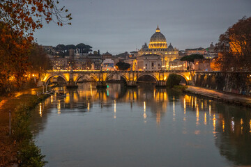 View over the Tiber River in a historic city. The old well-known bridge Ponte Sant'Angelo, in the evening. Rainy weather at sunset and view of the Basilica di San Pietro, Rome, Italy