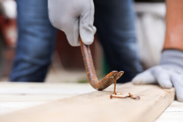 Sticker - Man pulling metal nail out of wooden plank with crowbar outdoors, closeup. Space for text