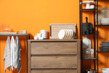 Wall Mural - Storage stands and chest of drawers with kitchenware near orange wall indoors