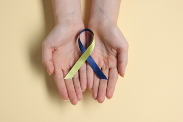 Canvas Print - Woman with yellow and blue ribbon on beige background, top view. Down syndrome awareness