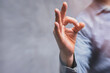 © vadish - Close-up of a man in a shirt shows hand gesture OK against a concrete wall.