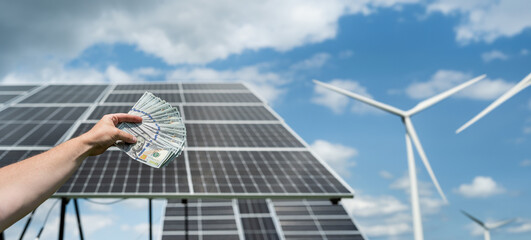 Poster - hand with dollar as saving against solar panels with wind turbines