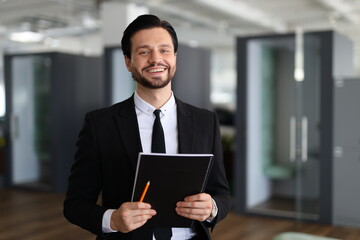 A man in a suit holding a clipboard and a pencil. He is smiling and he is happy