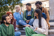 © Lomb - Diverse students socializing outdoors, multicultural group using smartphones on campus steps