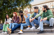 © Lomb - Diverse students socializing outdoors, multicultural group using smartphones on campus steps