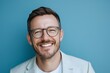 © Julian Adams - A Happy Man Smiling Against a Blue Background, Wearing Glasses and a Light Blazer His Joyful Expression Conveys Positivity and Confidence, Ideal for Lifestyle and Fashion Themes