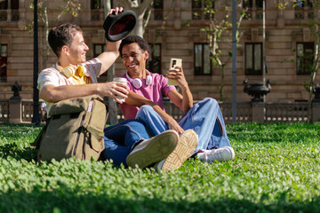 a multiethnic couple of two young men are sitting in a grassy park in the city.