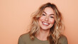 © Curioso.Photography - Smiling woman with wavy blonde hair standing against a light orange background.