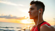 © Sergey - Close up young strong sporty toned fit sportsman man wear sports clothes listen to music in earphones warm up training at sunrise sun dawn over sea beach outdoor on pier seaside in summer day mornin