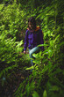 © Michael - Female tourist wearing a hard shell rain jacket walks up a forest path with ferns in a wet rainforest. Poco dos Pulgas waterfalls, Madeira, Portugal, Europe.