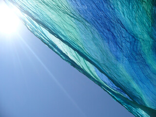 Sun with its rays, blue sky and delicate, airy, blue and turquoise material wrinkled in wind. Topics: weather, wind, atmosphere, sky space, season, sunny season, vacation, relaxation, rest, peace