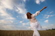 © Michalis Palis - Young woman wearing white dress dancing outdoors against blue cloudy sky.