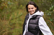© PeterPike - Young beautiful smiling dark-haired girl in vest and hoodie standing against blurred forest background. Concept of unity with nature