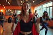 © keiron - Group of smiling women in creative Halloween costume superhero cape, fun fitness class lifting weights, aerobics session