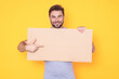 © Volodymyr - Guy with blank banner ad, isolated on studio background. Man holding empty blank poster showing placard pointing finger and gesturing index finger on board. Male presenting signboard or banner.