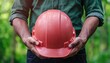 © WinThing - Person holding a red hard hat in forested surroundings.