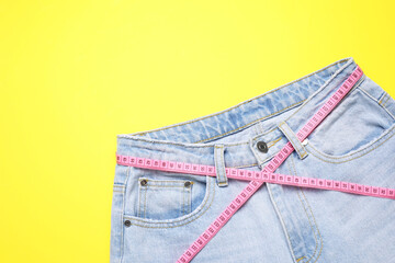 Canvas Print - Jeans and measuring tape on yellow background, top view