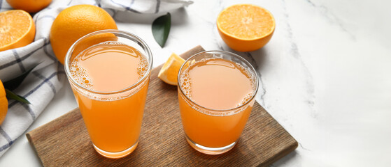 Wall Mural - Wooden board with glasses of tasty juice and fresh oranges on white marble background