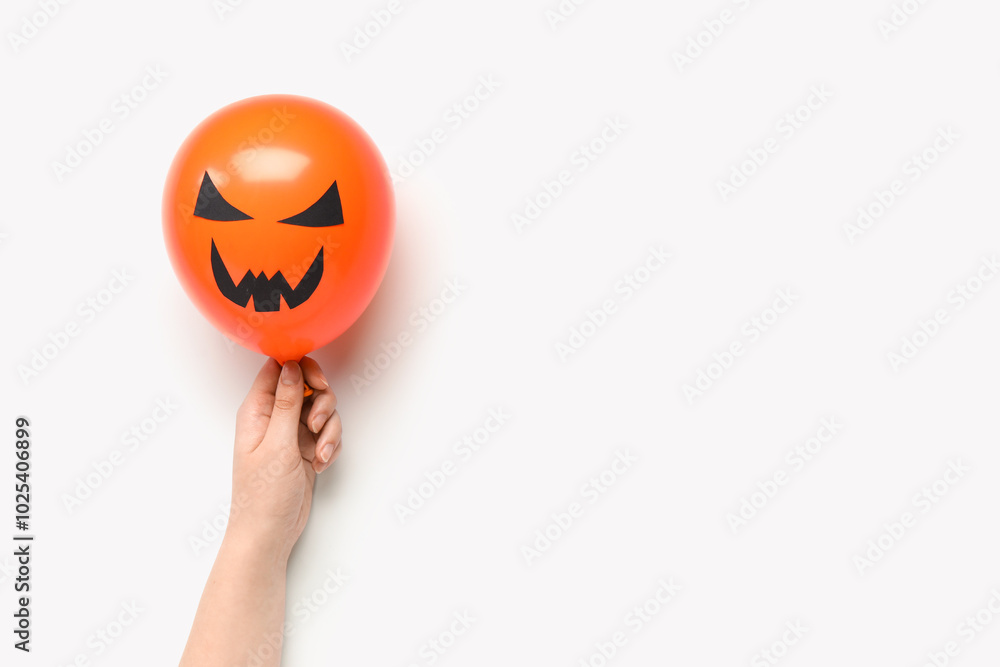 Female hand with funny Halloween orange balloon on white background