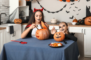 Wall Mural - Little girl with her mother carving Halloween pumpkin in kitchen