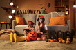 © Pixel-Shot - Little girls dressed for Halloween with toy spider and card at home in evening