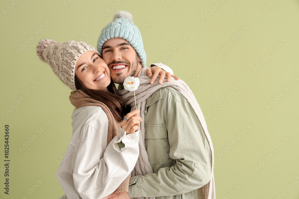 Loving couple in winter clothes with lollipop hugging on green background