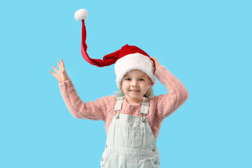 Wall Mural - Cute little girl in Santa hat on blue background