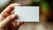 © Arifin Studio - A hand holding a blank white business card with a blurred background.