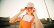 © Flashizzle/peopleimages.com - Bridge, woman and portrait with sunglasses for fashion, streetwear and confidence for cool clothes with pride. Urban, female person and smile with positivity for hipster, trendy hat and gen z in city