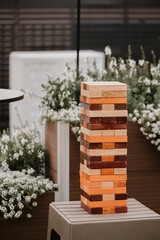 Large wooden Jenga tower on an outdoor table, surrounded by flowers