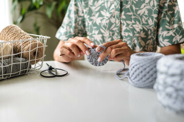 Close up female hands. Girl crochets from gray cotton yarn. Skeins of natural, natural colors