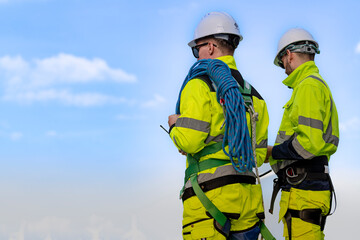 two engineers in high visibility jackets and helmets are inspecting a wind farm. one is holding a mo