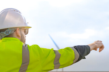 two engineers in high visibility gear and hard hats observe a wind turbine and communicate via radio