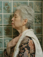 Sticker - A woman with grey hair and a towel around her neck stands in front of a tiled wall. AI.