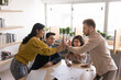 © fizkes - Happy successful diverse team of young coworkers enjoying successful teamwork, group achievement, startup project success, giving high five over meeting table smiling, laughing, clapping hands