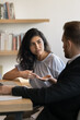 © fizkes - Serious young Indian manager woman talking to boss at workplace table, consulting business legal expert, lawyer in formal suit. Diverse colleagues talking at workplace. Vertical shot