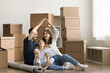 © fizkes - New home. Excited laughing family couple with preteen age kid first time buying house celebrate moving in sit on floor among boxes with stuff having fun make roof of hands above heads. Copy space