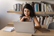 © fizkes - Focused pensive young adult Indian entrepreneur woman sitting at computer in library, reading online content on screen, analyzing information, working on learning project, research study