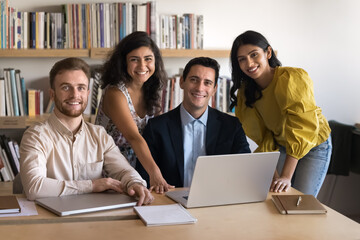 Sticker - Multiethnic team of happy young Indian and Latin coworkers posing for portrait in office library. Diverse business colleagues meeting at laptop, looking at camera, smiling, enjoying teamwork