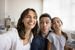 © fizkes - Funny selfie. Joyful family young parents preteen age child girl shoot cute self photo portrait videocalling by phone laugh grimacing making hilarious faces having fun on couch at living room together