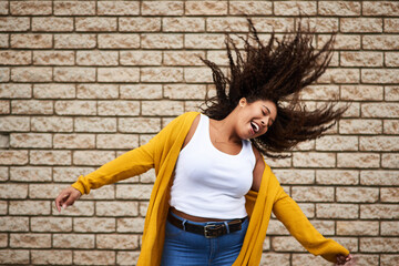 Happy, woman and dancing with hair flip for playful movement, energy and fun celebration of fashion winner. Excited, girl and rhythm for success, freedom and deal achievement on brick wall background