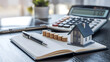 © Rsquare stock - tax day background,House model, house placed on a white surface, next to a calculator, a pencil, and some coins, symbolizing home finances, budgeting, or real estate planning.