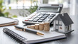 © Rsquare stock - tax day background,House model, house placed on a white surface, next to a calculator, a pencil, and some coins, symbolizing home finances, budgeting, or real estate planning.