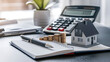 © Rsquare stock - tax day background,House model, house placed on a white surface, next to a calculator, a pencil, and some coins, symbolizing home finances, budgeting, or real estate planning.